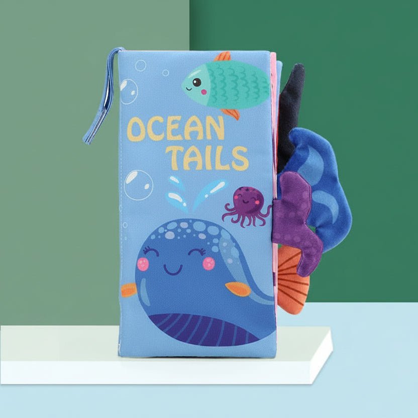 Children's soft book titled 'Ocean Tails' with ocean-themed illustrations on a green and blue gradient background.